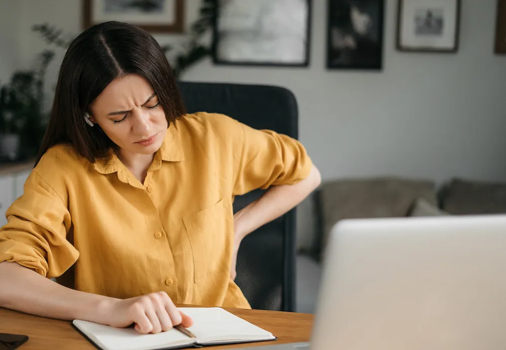 Woman suffering from back pain caused by poor posture while working at a desk