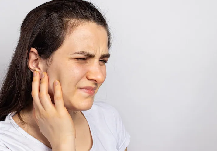 Woman experiencing pain near the jaw joint and ear due to TMJ dysfunction before chiropractic treatment