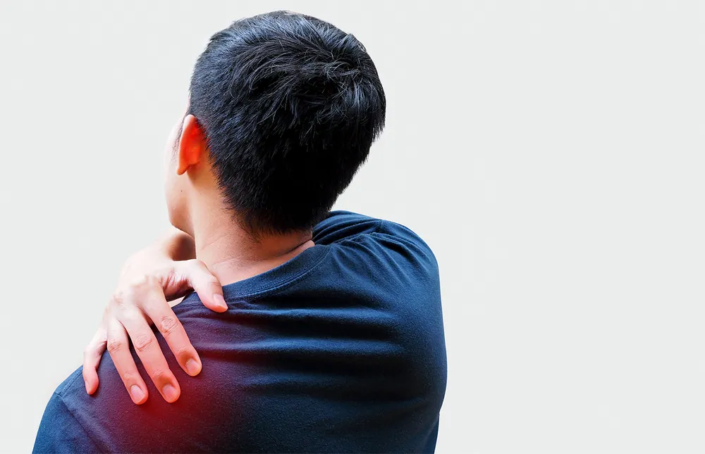 Rear view of a person holding a painful shoulder and upper back due to shoulder joint dysfunction treated with chiropractic care